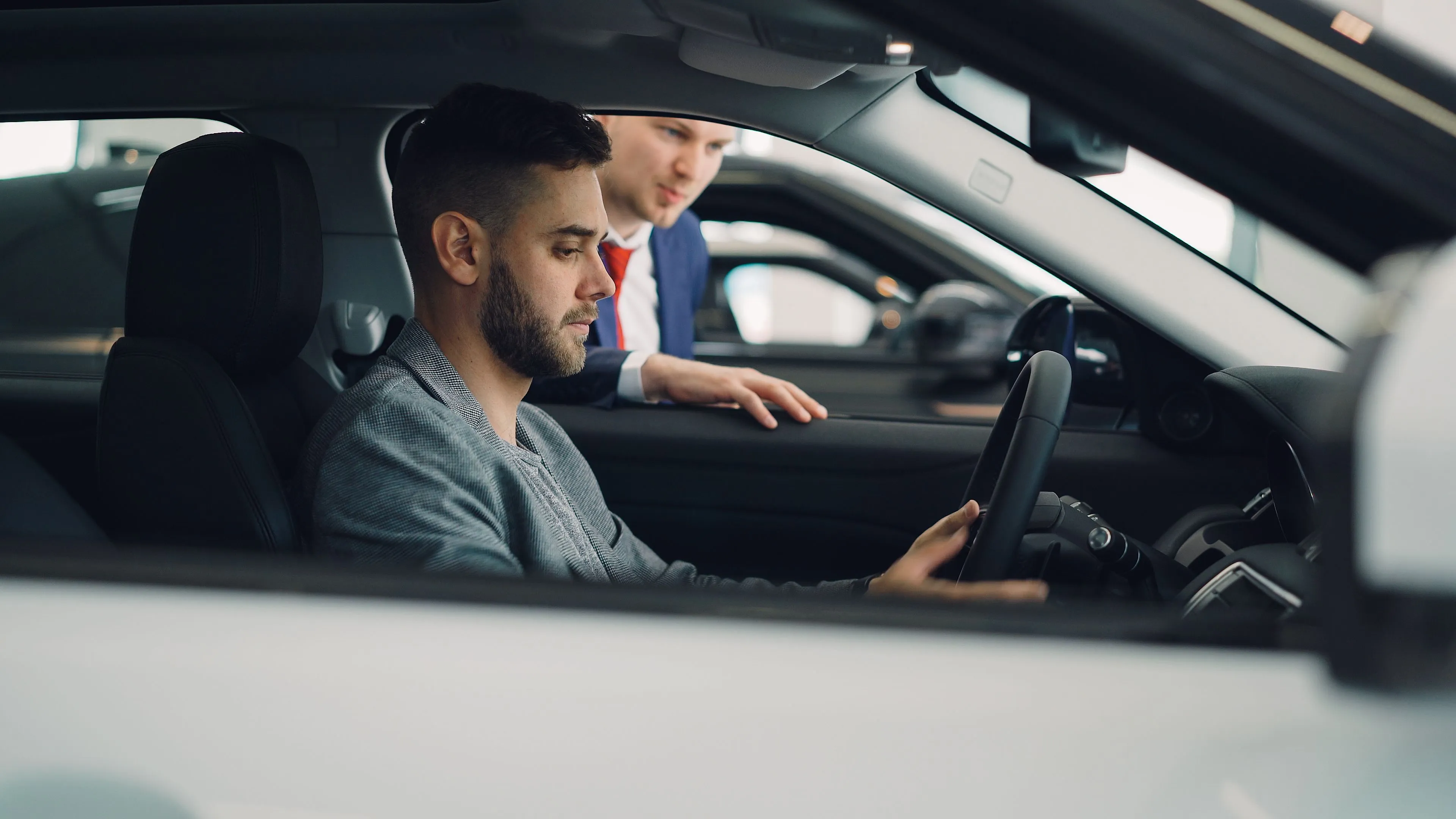 Joven probando un coche en un concesionario mientras un vendedor le asesora
