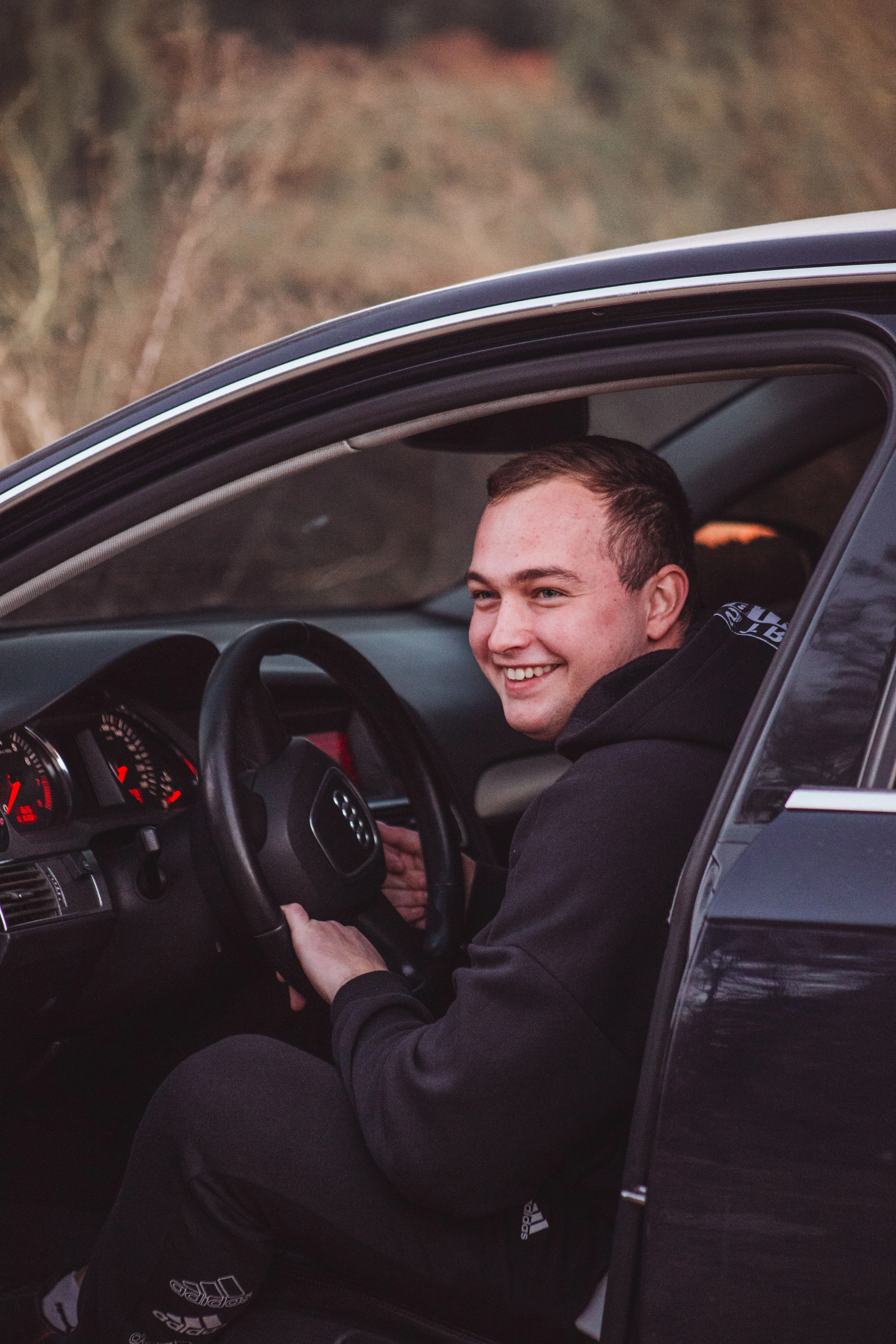 Joven conductor novel sonriente al volante de su coche con la puerta abierta
